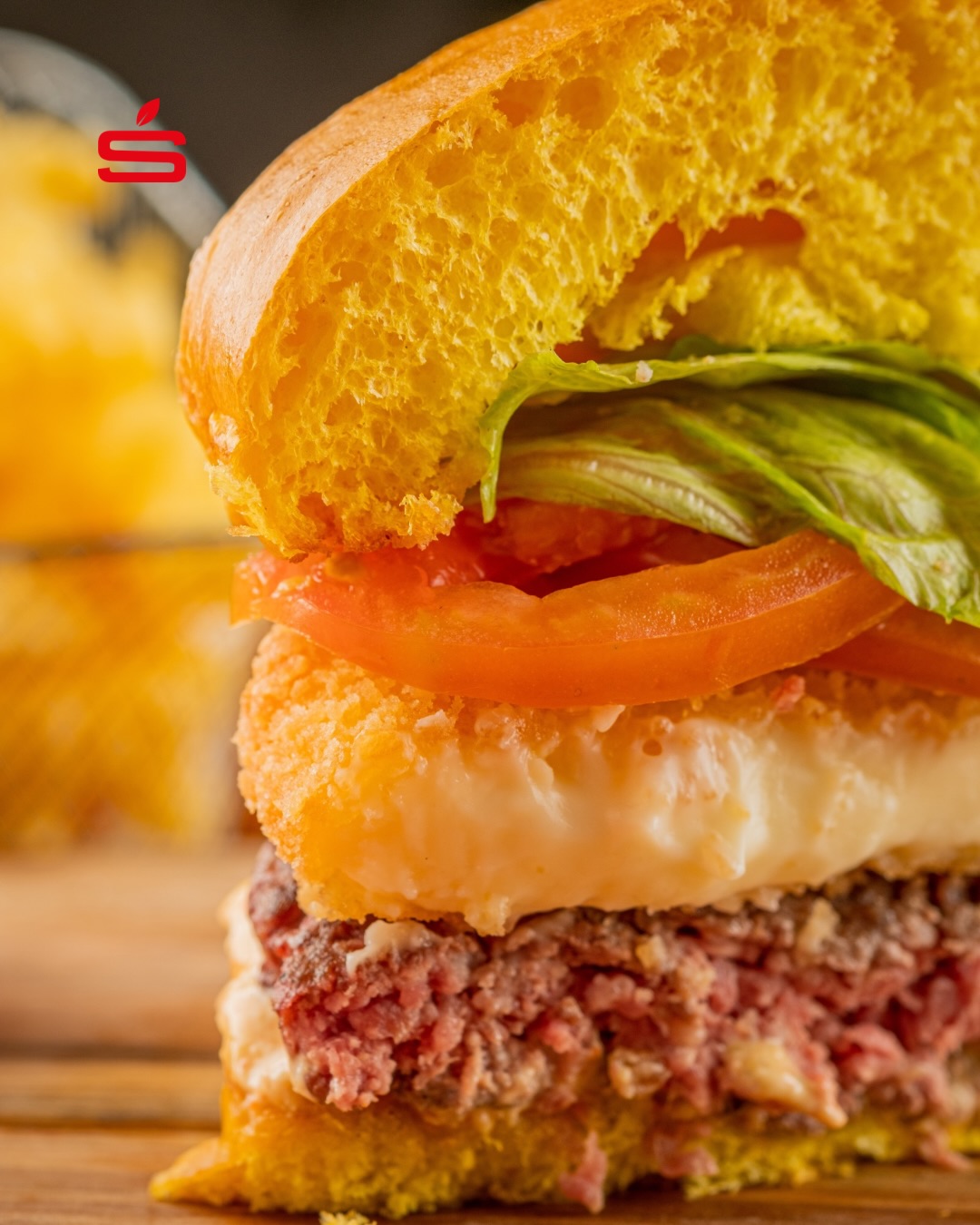 Close de hambúrguer artesanal da STARV com queijo empanado, tomate e alface