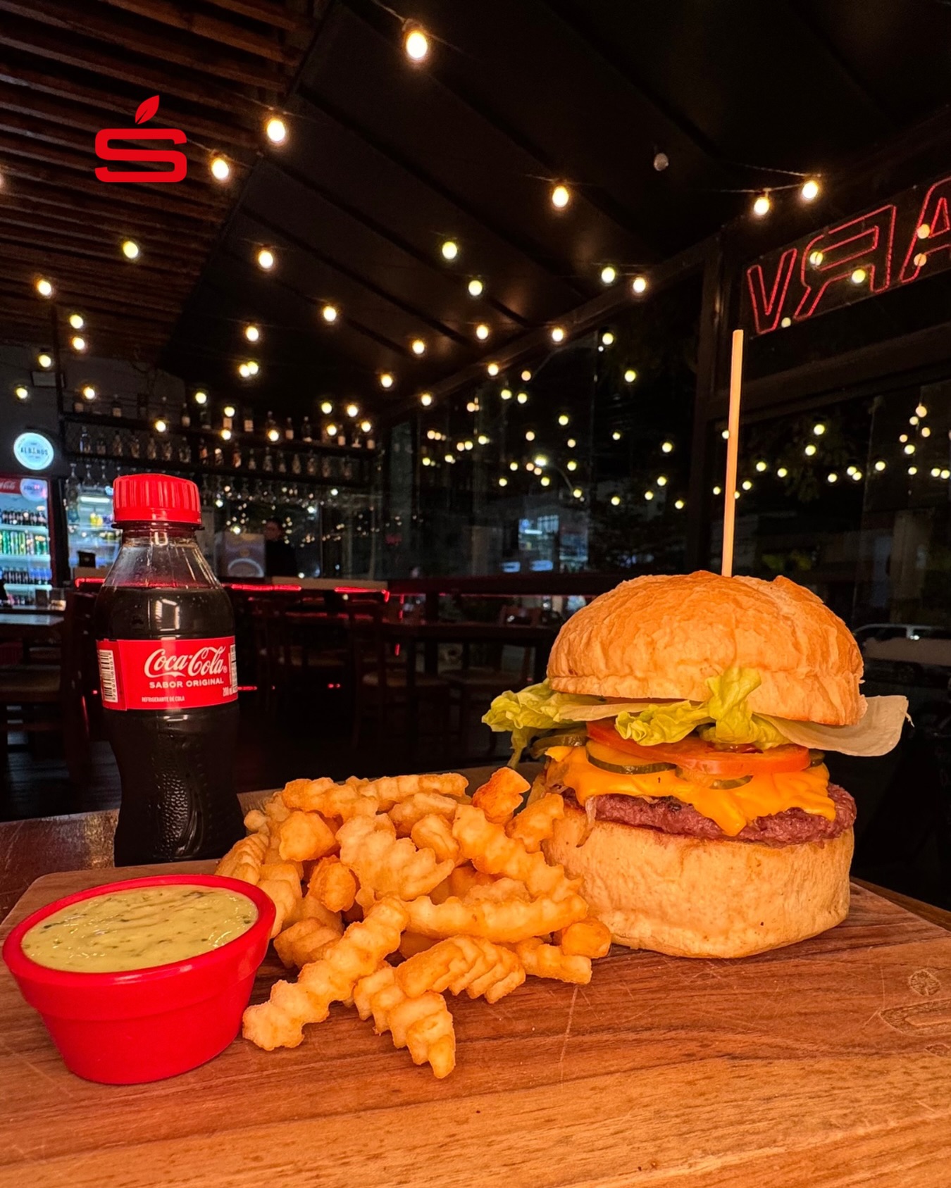 Hambúrguer com fritas e Coca-Cola na mesa da STARV, com luzes ao fundo